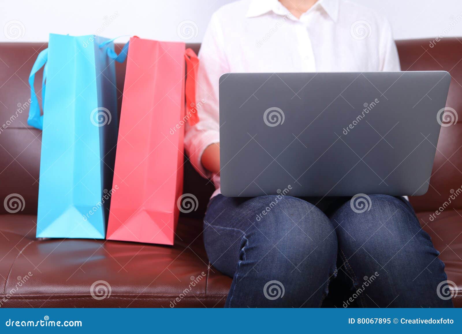 woman sit on sofa with shooping bag beside and using laptop