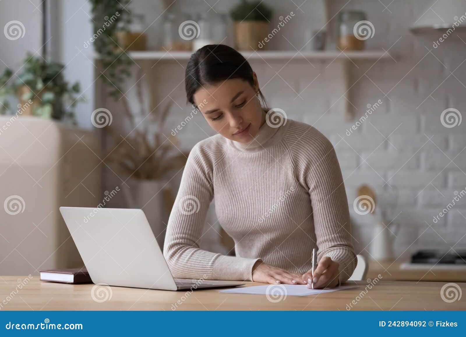 woman sit at table with laptop jotting information on paper