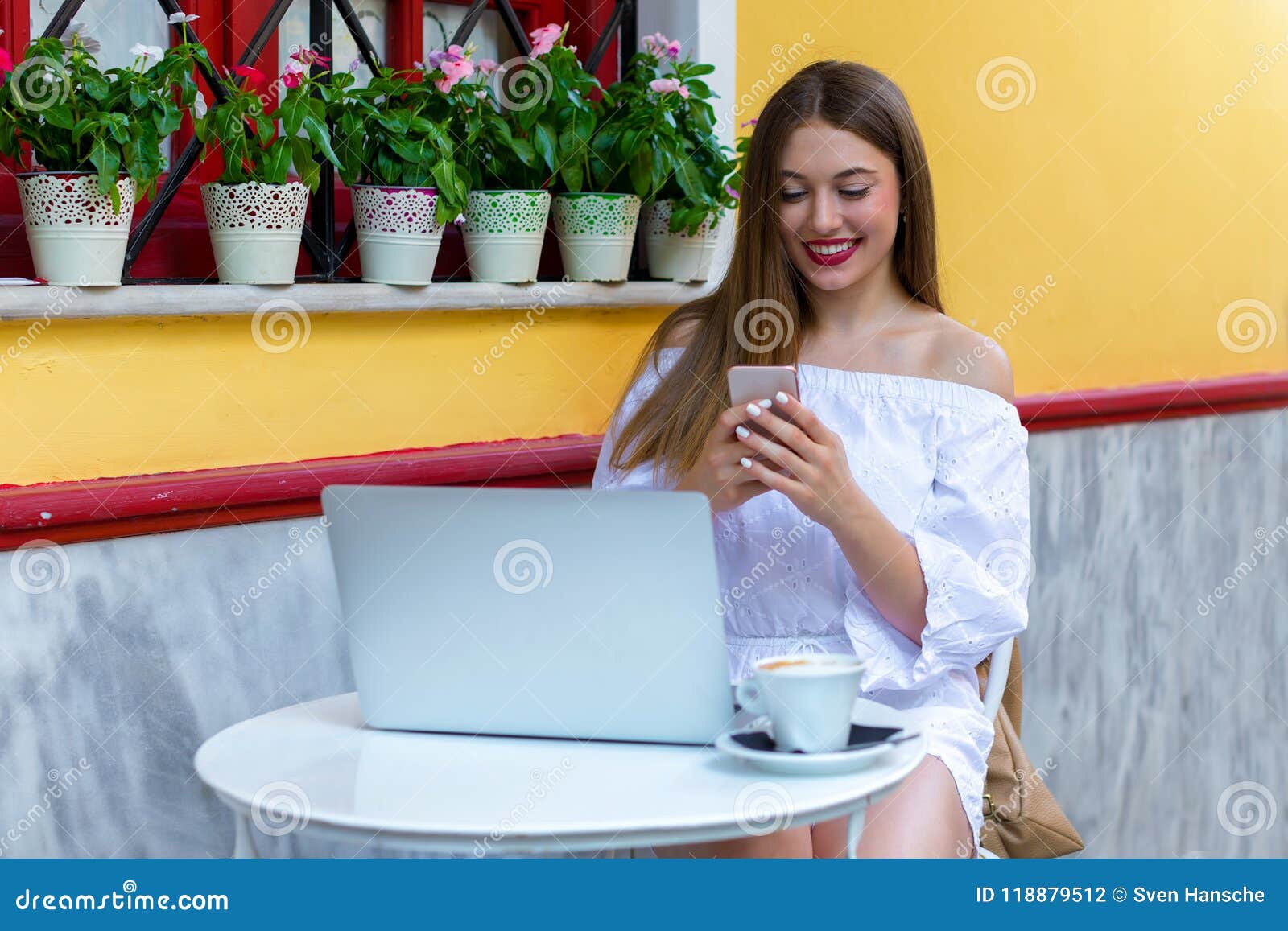 woman sits in a brasserie and works on laptop and smartphone