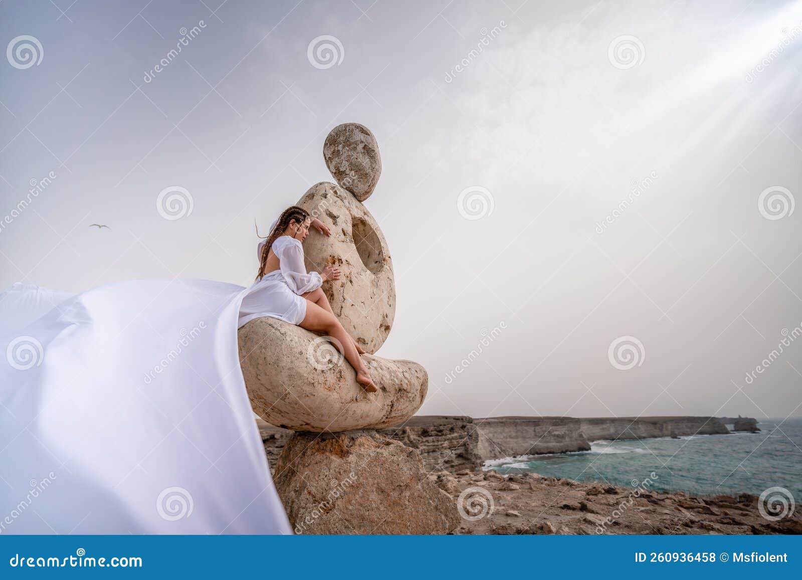 A Woman Sits on a Stone Sculpture Made of Large Stones. she is Dressed ...