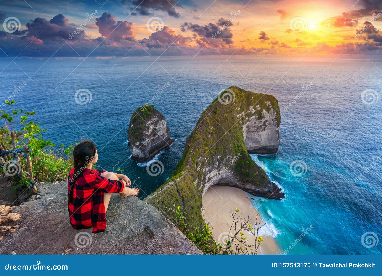 woman sitting on cliff and looking at sunset at kelingking beach in nusa penida island, bali, indonesia.