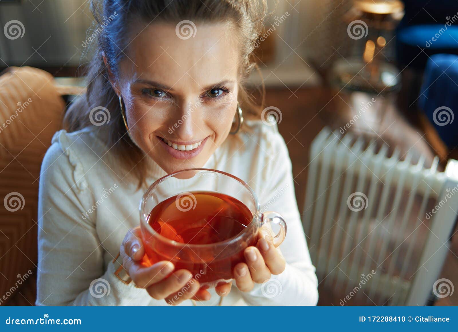 Woman Sitting on Couch Near Oil Radiator and Drinking Tea Cup Stock ...