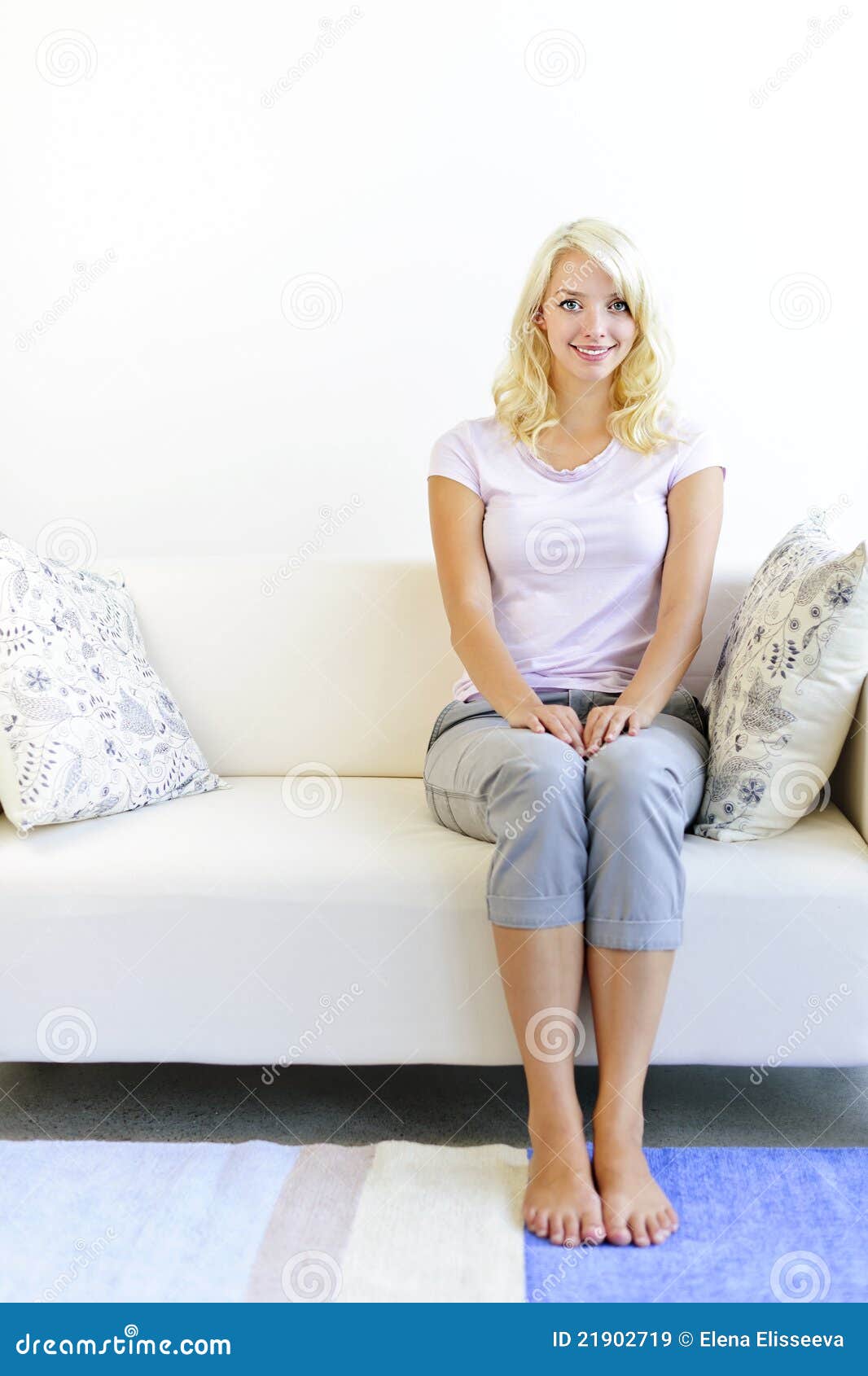 Woman sitting in living room. Pretty blonde woman sitting on sofa at home smiling