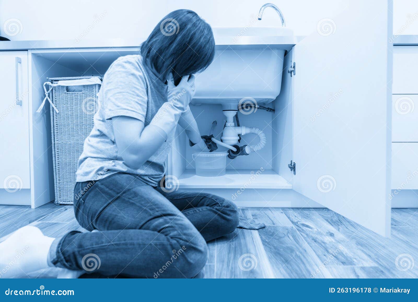 Woman Sitting Near Leaking Sink in Laundry Room Calling for Help Stock