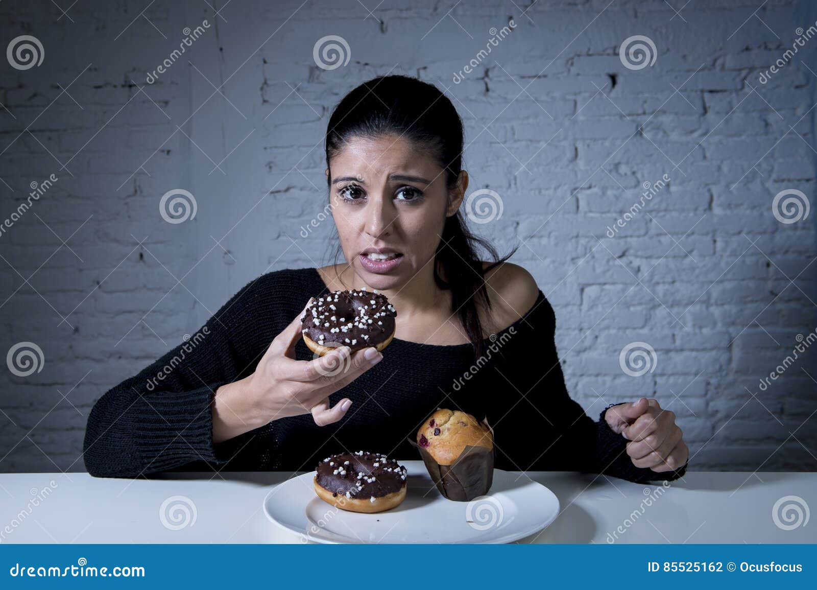 woman sitting at table feeling guilty forgetting diet eating dish full of junk sugary unhealthy food