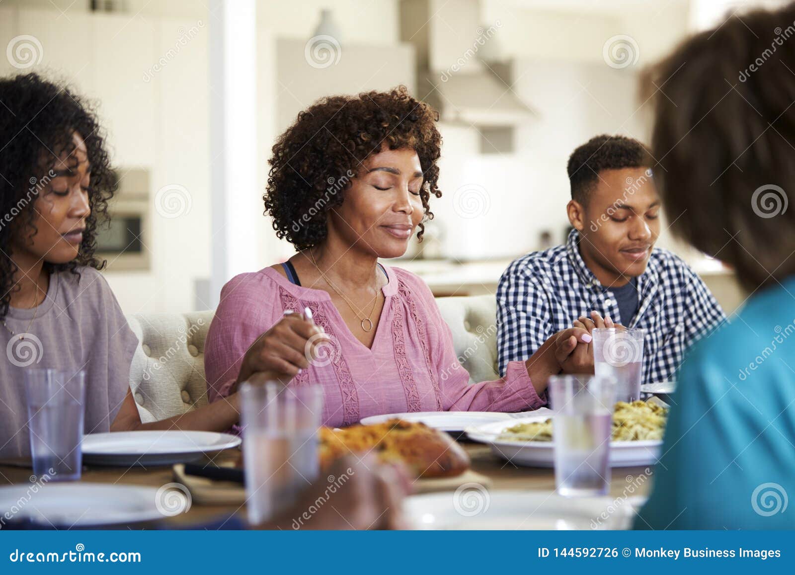 woman sitting at the table holding hands with her young adult children saying grace before dinner