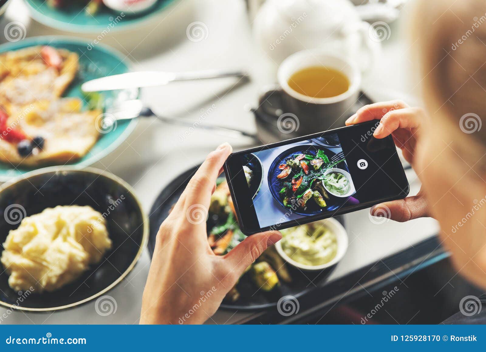 woman with smart phone taking picture of food at restaurant