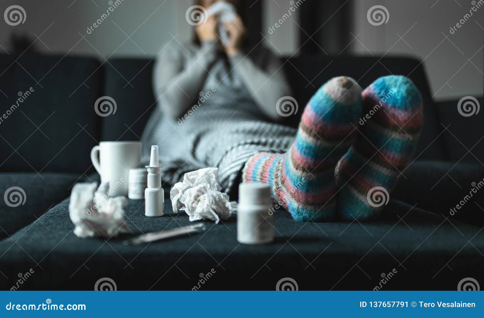 woman sneezing and blowing nose with tissue and handkerchief. sick and ill person with flu, cold medicine and woolen socks.