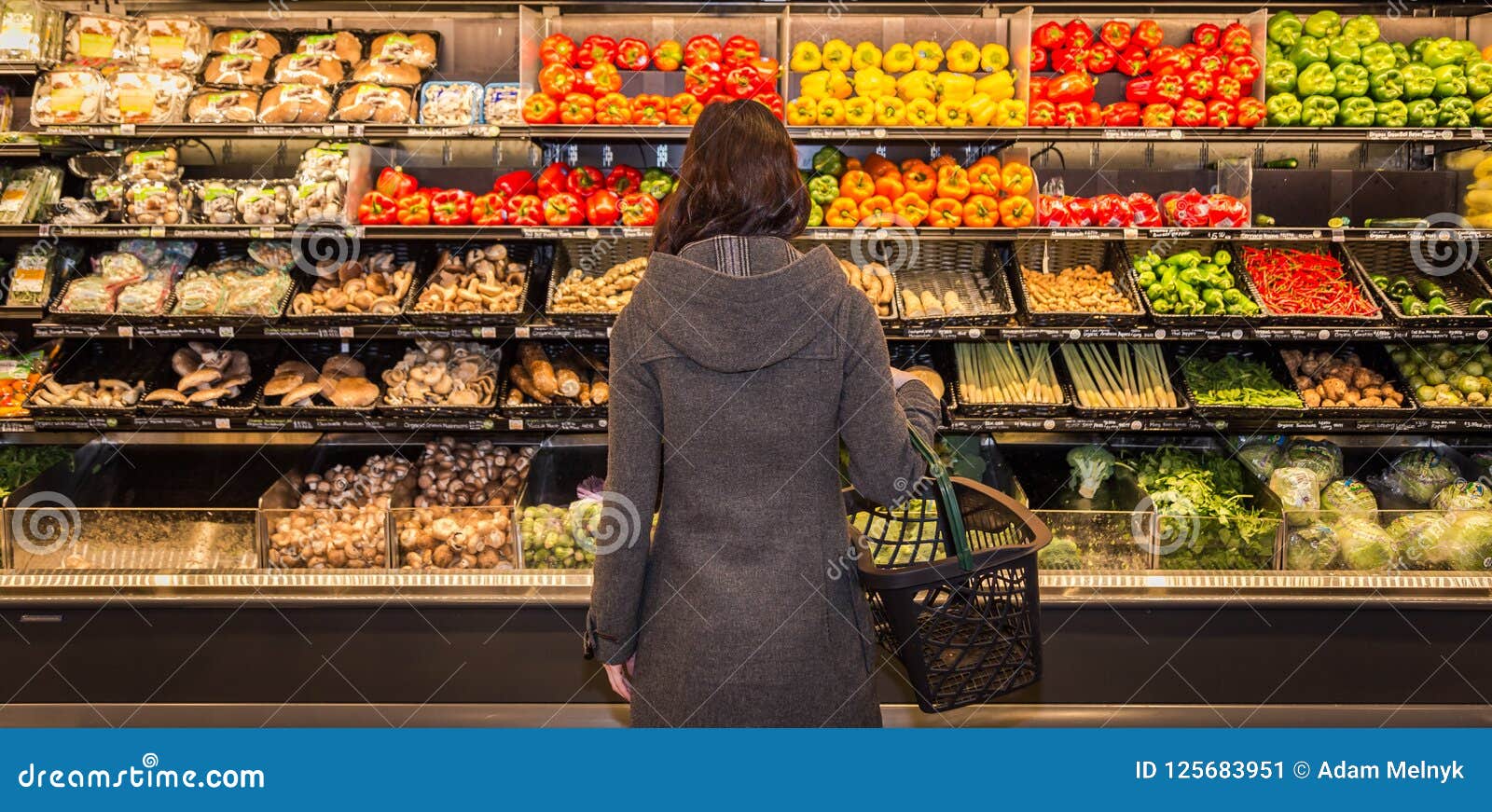 woman standing in front of a row of produce in a grocery store.