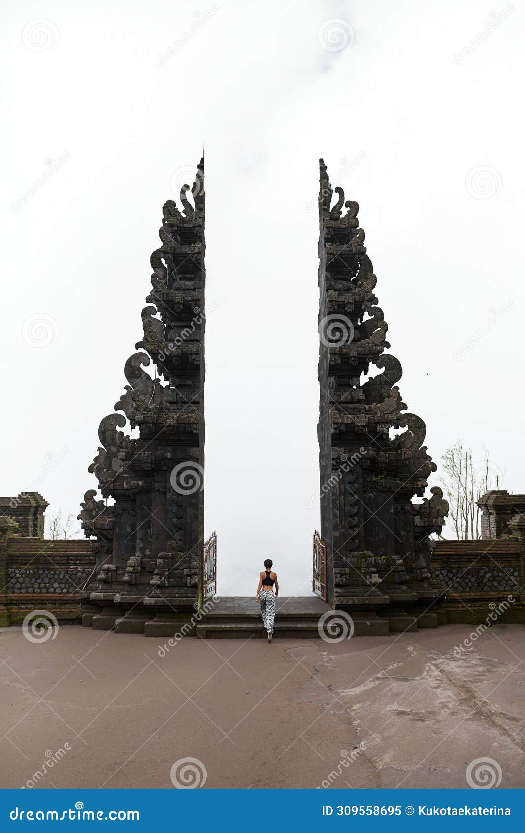 a woman stands at the balinese traditional gate in the clouds at the sacred temple of pura pasar agung sebudi on mount agung