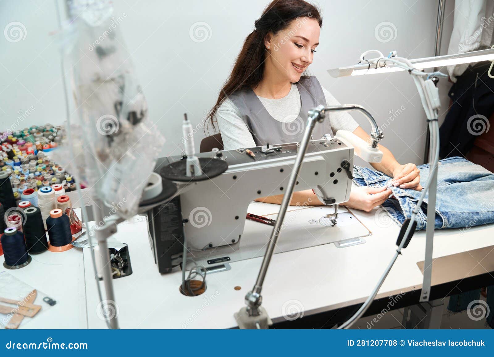 Woman Tailor Sewing Button Back on Denim Pants after Dry Cleaning