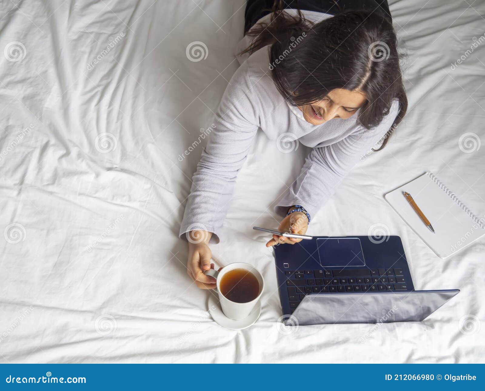 woman taking a call in pijama in bed drinking coffee in the morning.