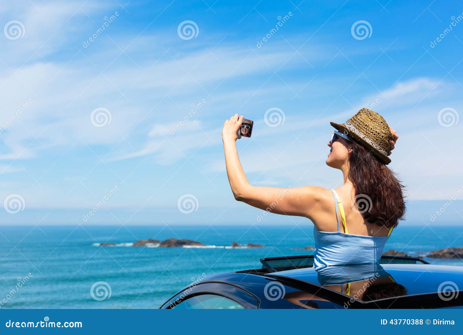 Smiling young couple taking selfie through mobile phone while standing in  car sun roof stock photo