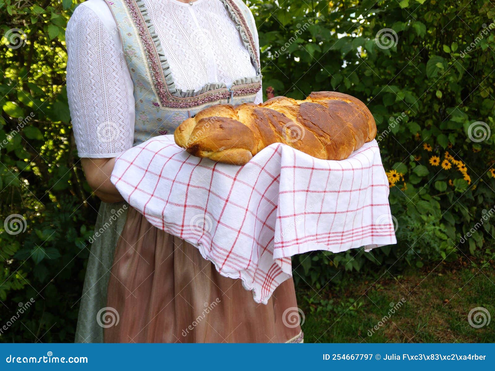 woman in traditional bavarian dirndl dress holding freshly baked loaf of rustic german bread (bavaria, germany)