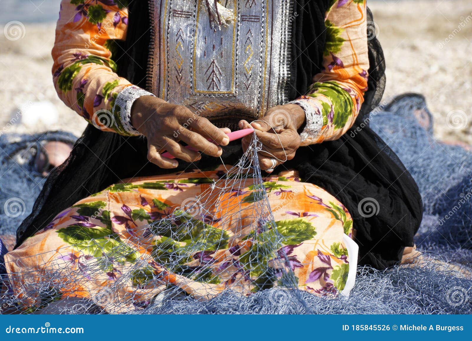 woman in traditional dress mending fishing net, oman