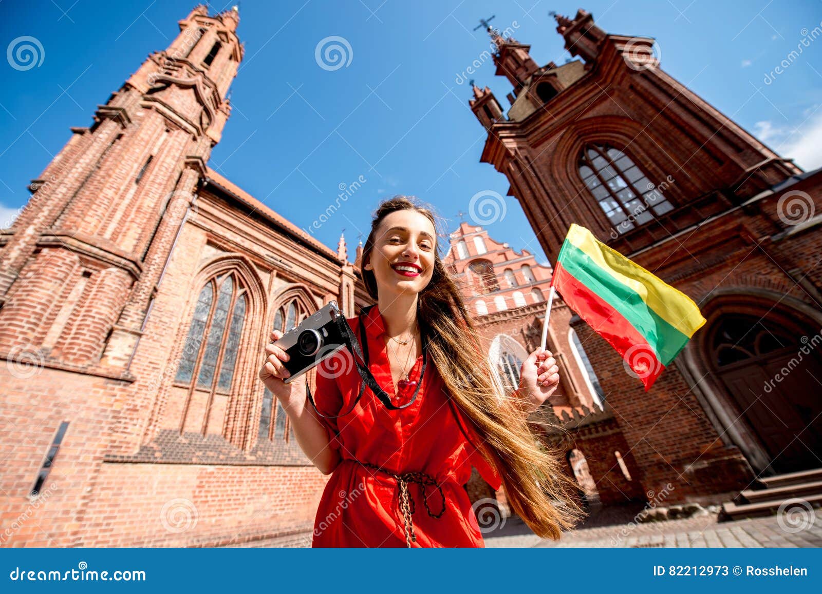 Woman traveling in Vilnius. Young female tourist with photo camera and lithuanian flag standing in front of the famous gothic church in the old town of Vilnius. Woman having great vacations in Lithuania