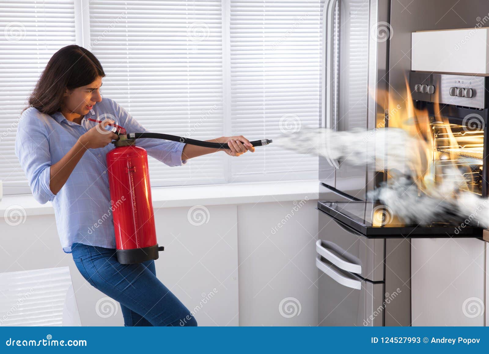 woman using fire extinguisher to put out fire from oven