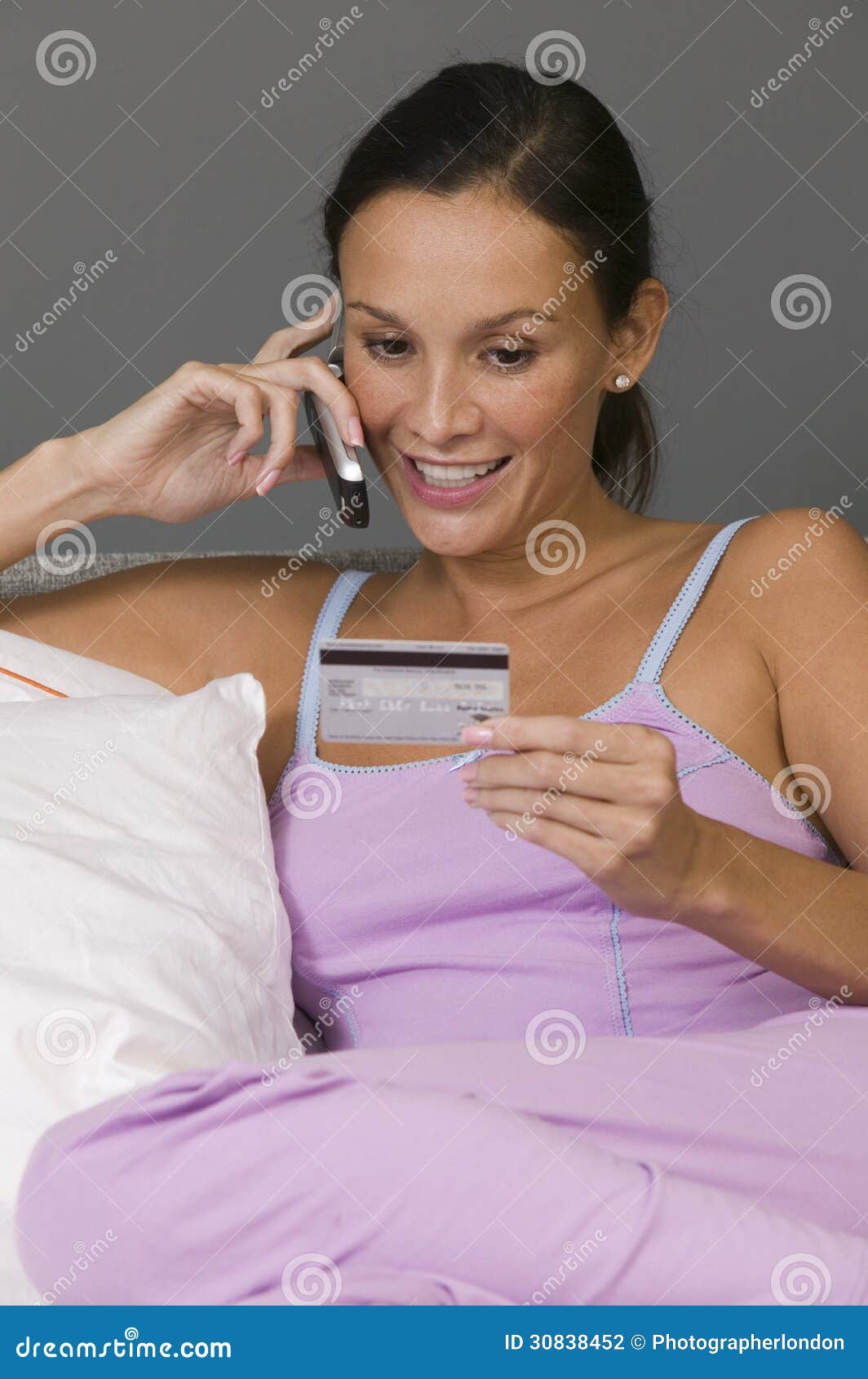 Woman Using Mobile Phone Making Credit Card Purchase Lying in Bed Stock