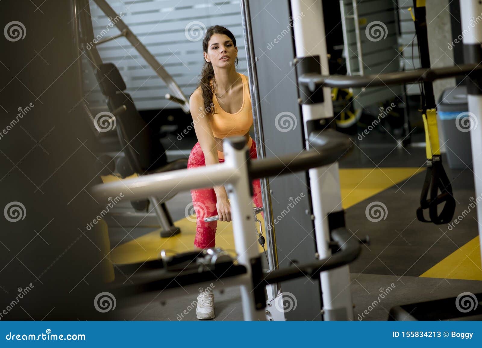 Woman Using Straight Bar Cable To Pull Up Weights To Exercise Biceps in