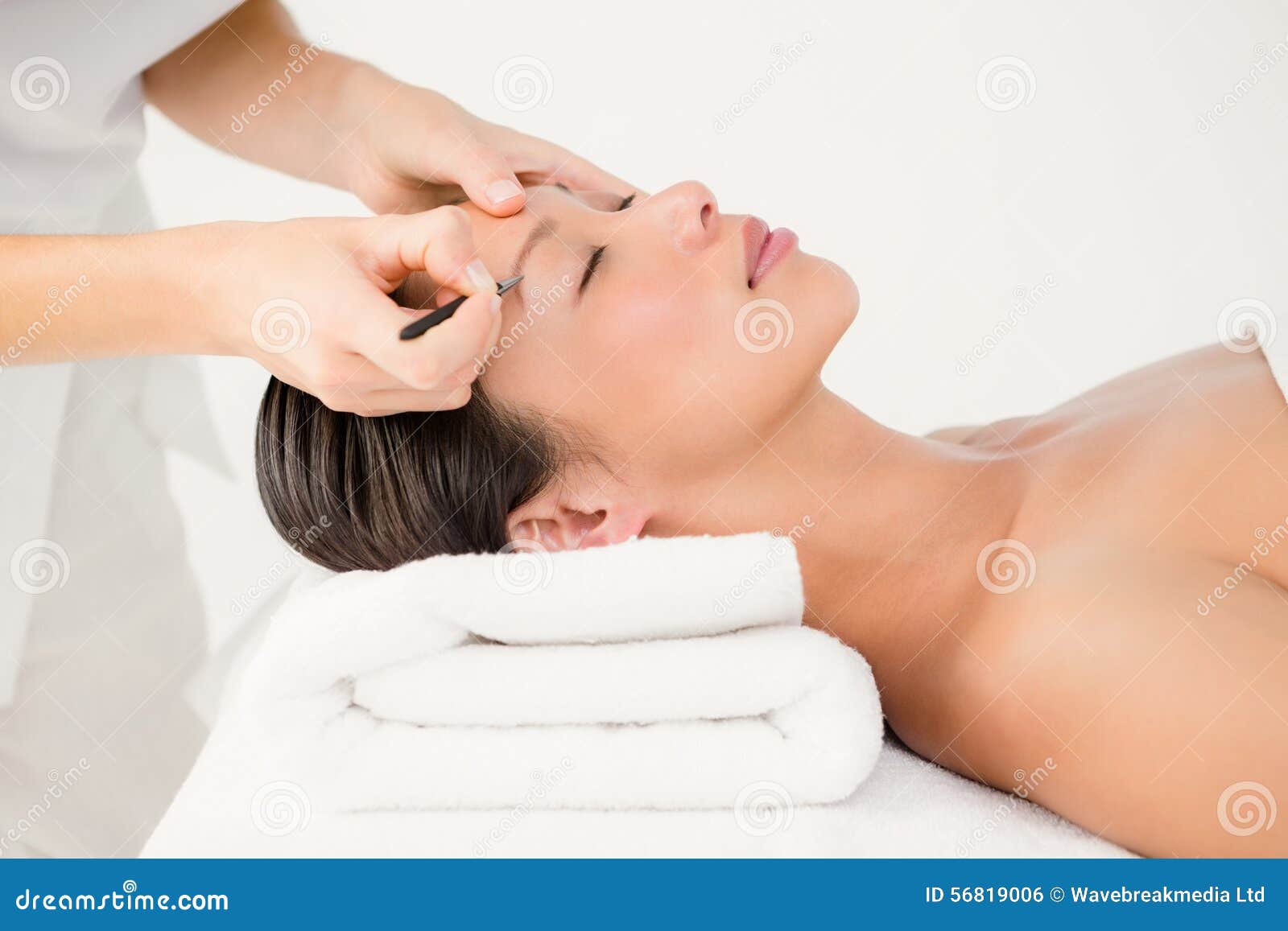 woman using tweezers on patient eyebrow