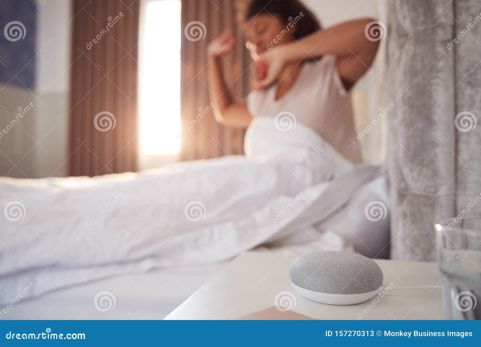 woman waking up in bed with voice assistant on bedside table next to her