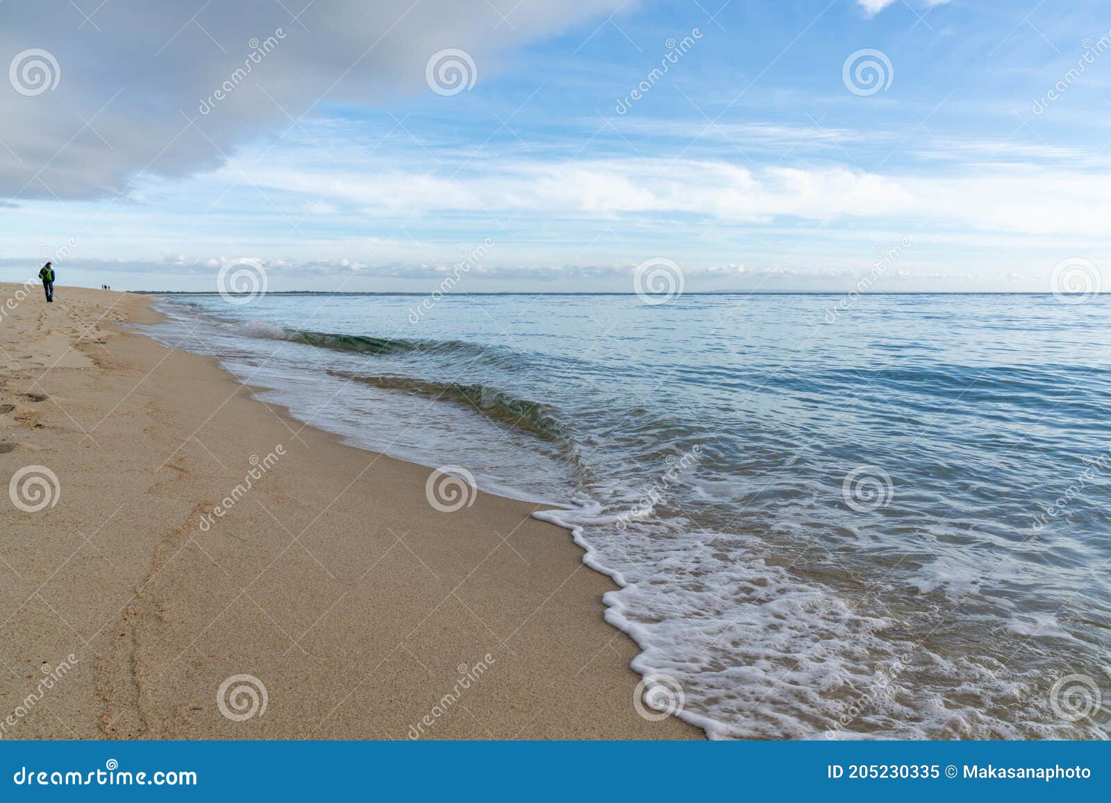woman walks along an endless golden sand beach with gentle waves