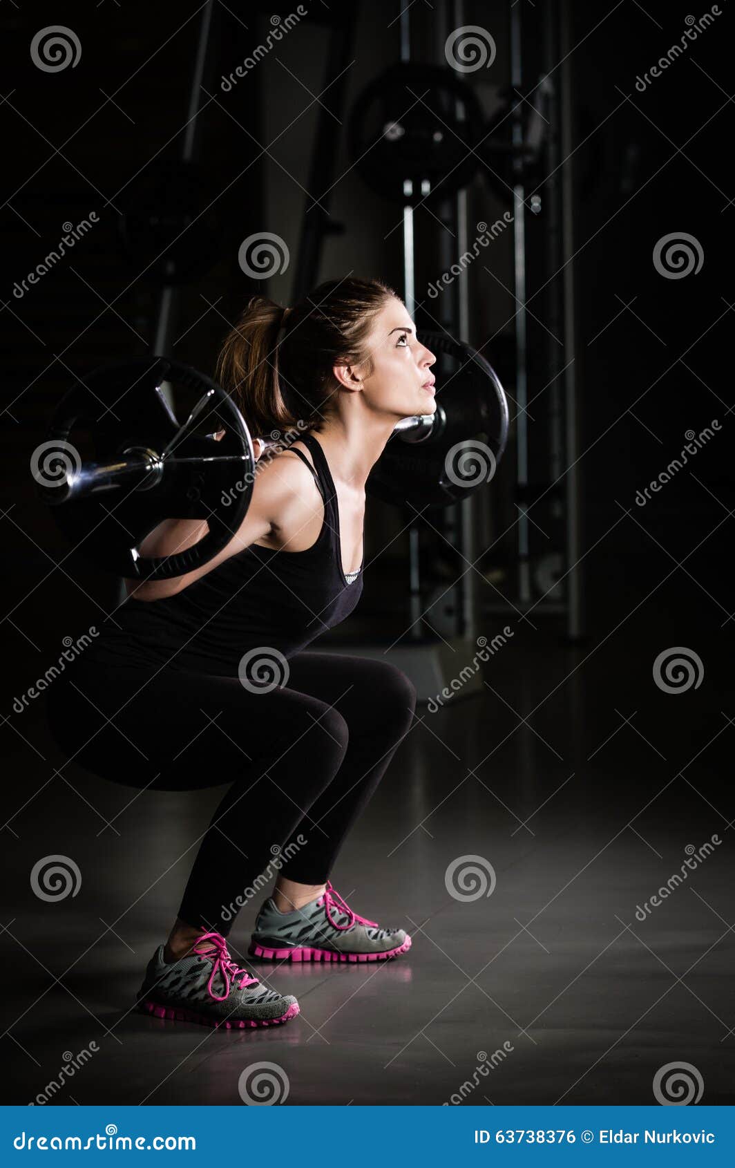 woman weight training at gym.devoted body builder girl lifting weights in gym and doing squats low key photo