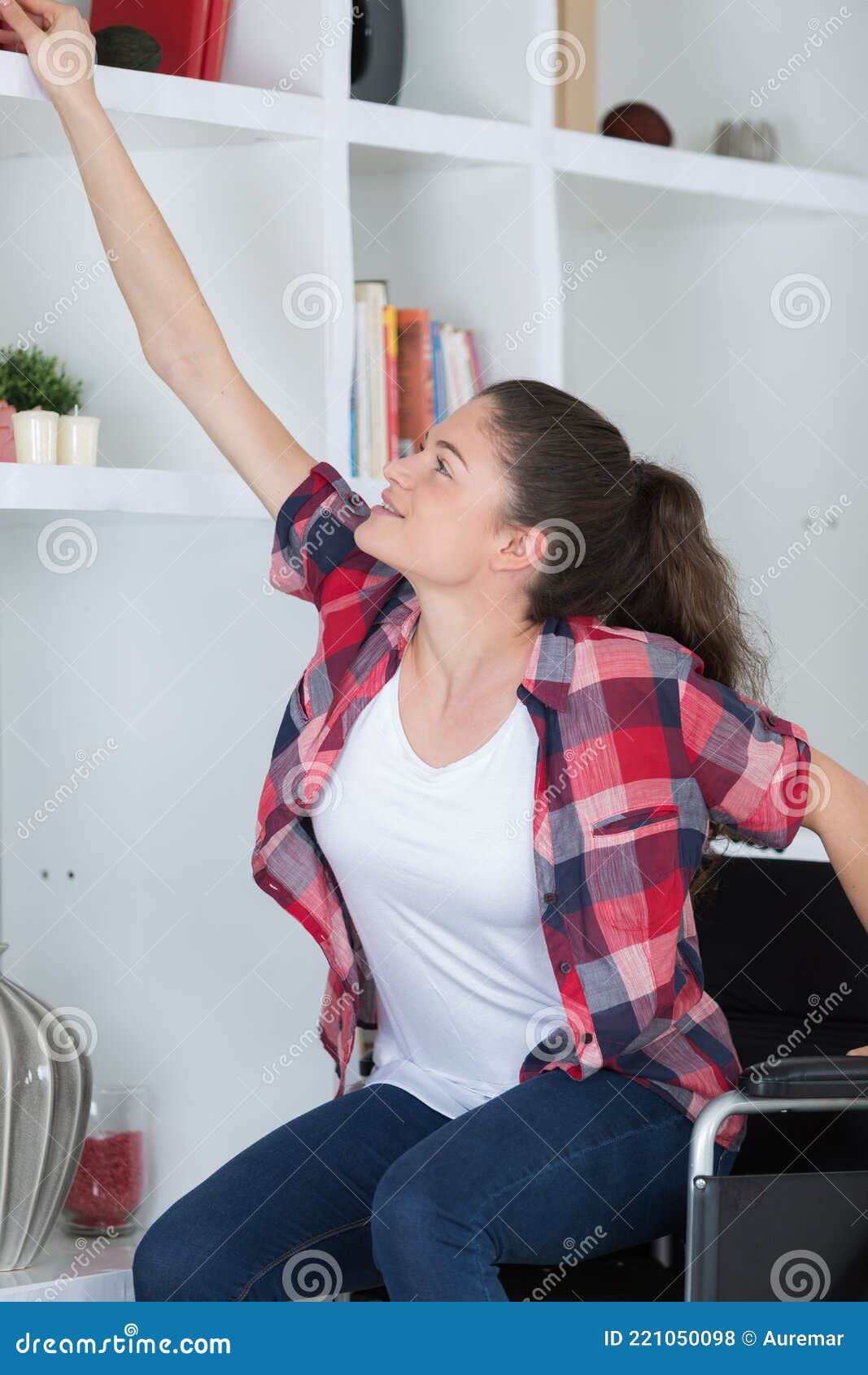 woman-in-wheelchair-reaching-for-something-from-living-room-shelf-stock