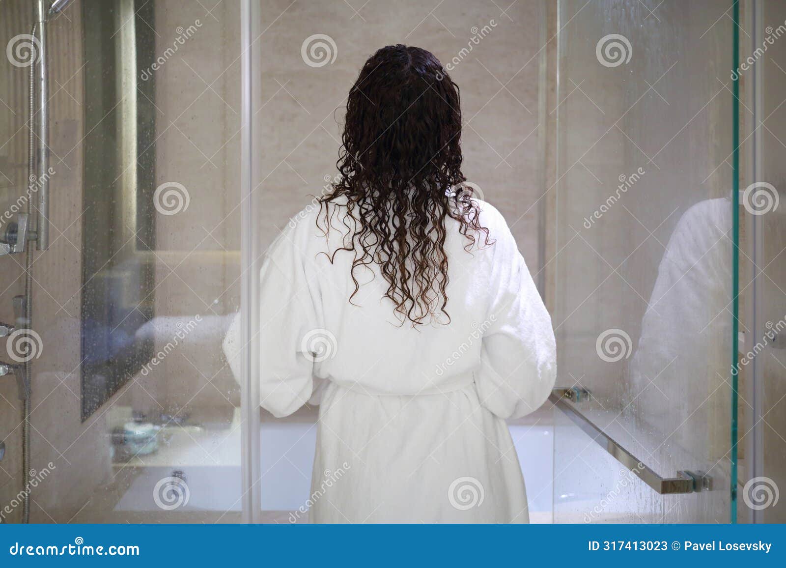 woman in white bathrobe enters bathroom with glass