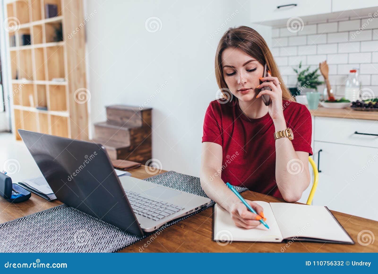 woman working at home write notes while talking on phone