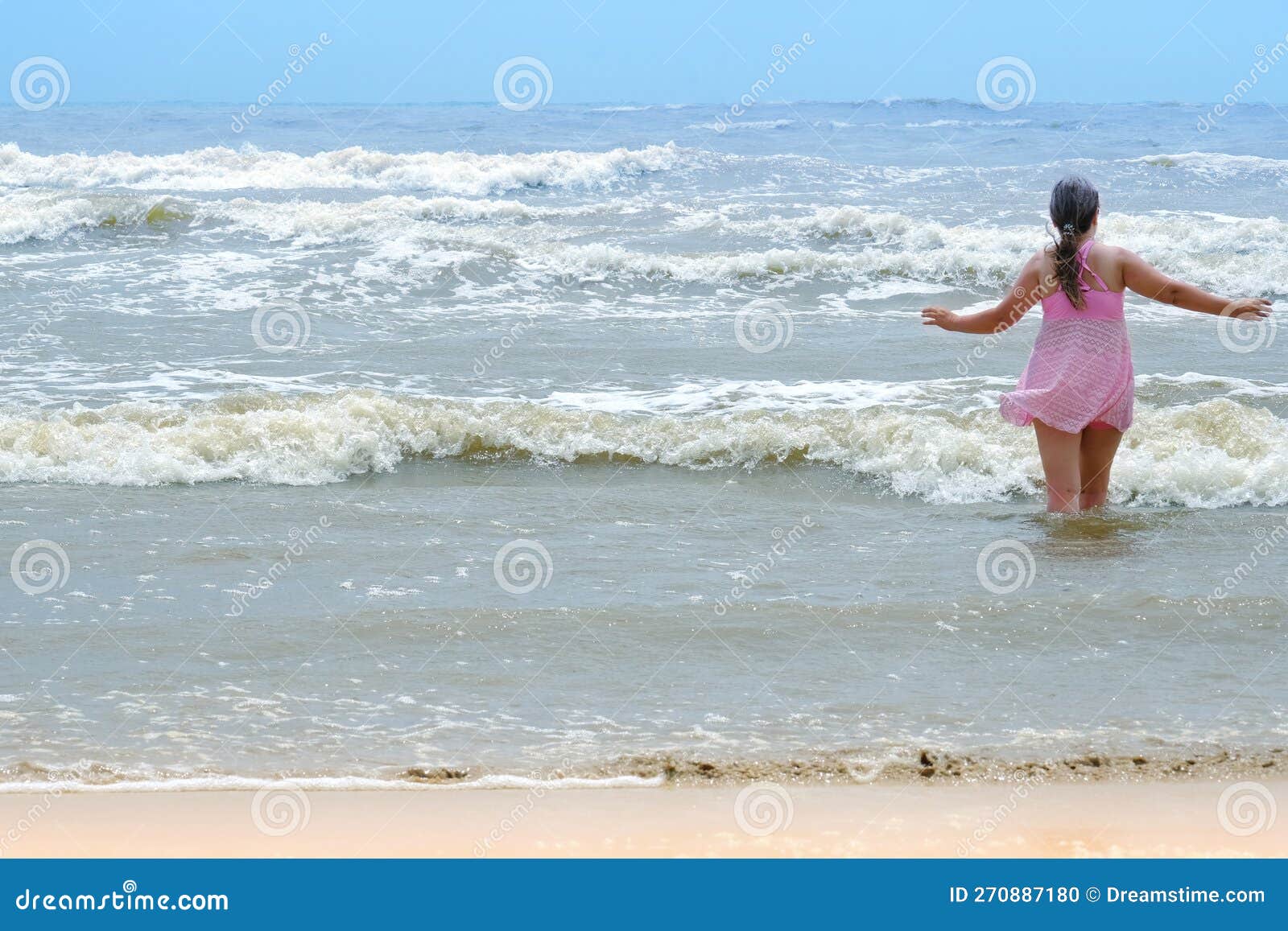 woman 50 years old with long hair in pink swimsuit with skirt enters water to swim, concept swim in waves, dangers of rip currents