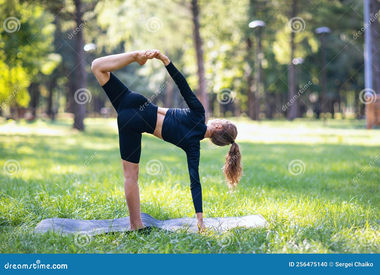 woman yoga practitioner performs variation ardha chandrasana exercise crescent pose trains park warm summer morning standing 256475140