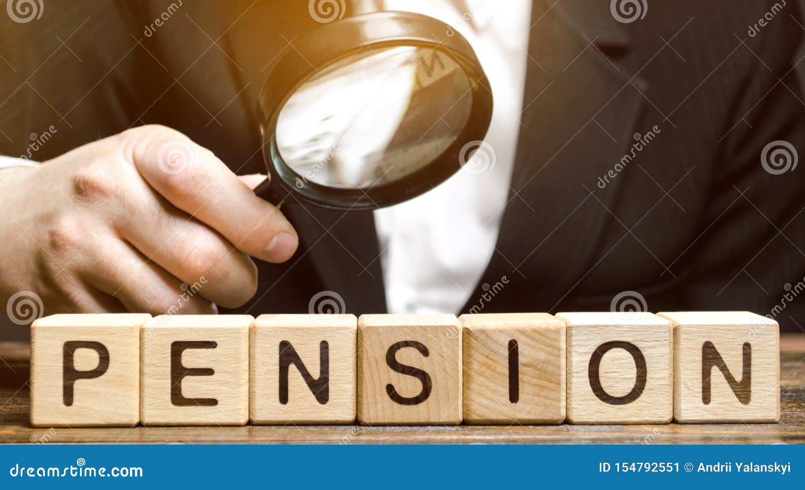 wooden blocks with the word pension and a magnifying glass in the hand of a man. analysis of retirement payments. the size of