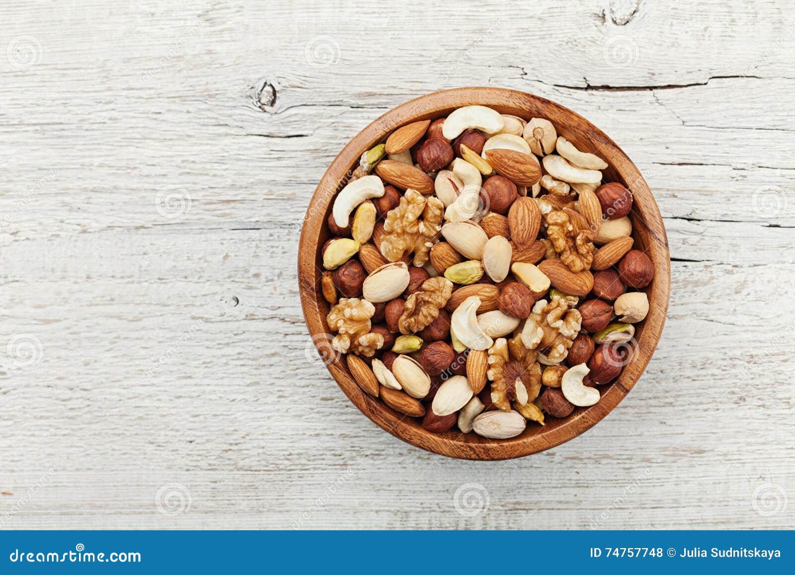 wooden bowl with mixed nuts on white table from above. healthy food and snack. walnut, pistachios, almonds, hazelnuts and