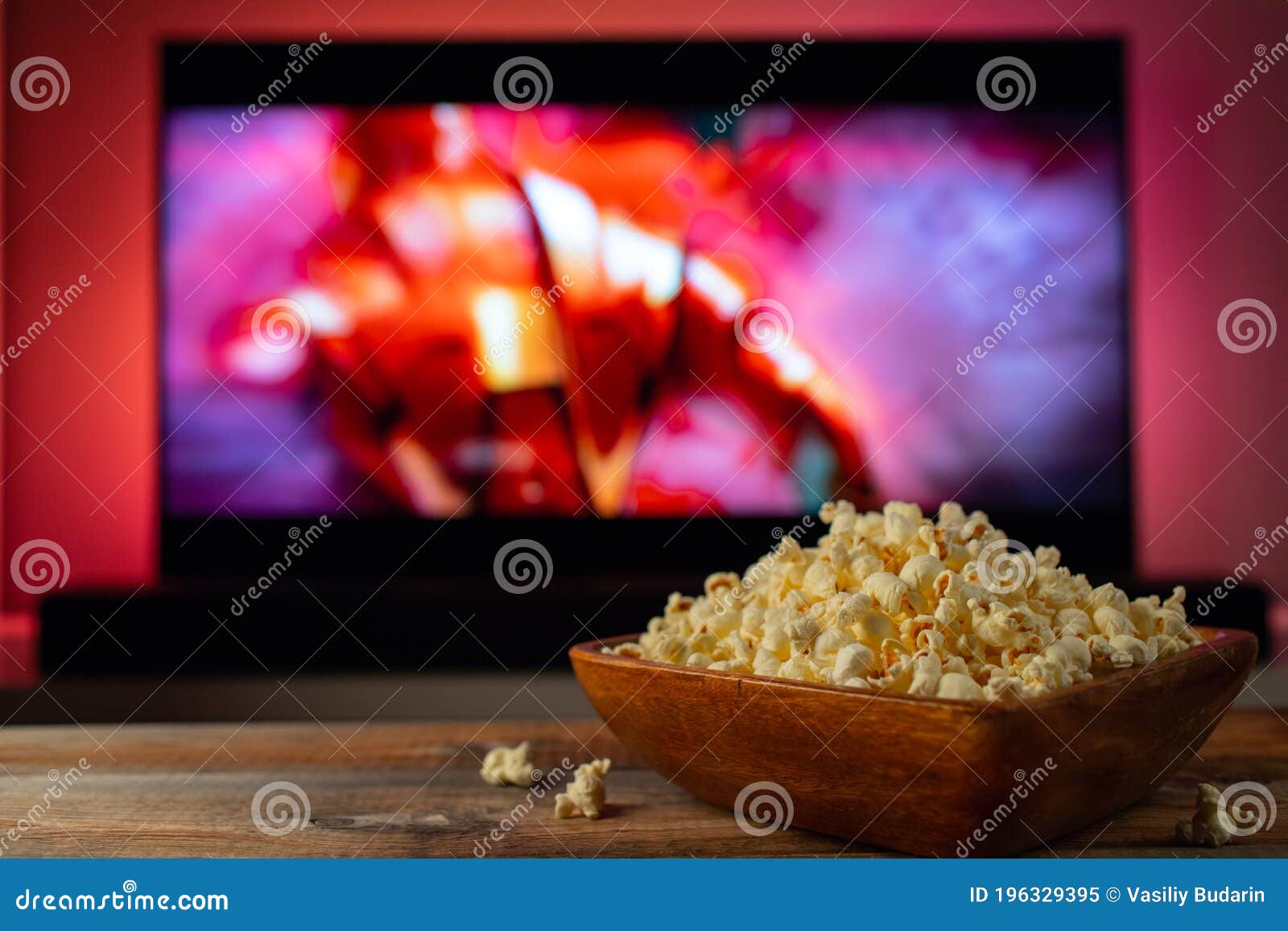 a wooden bowl of popcorn and remote control in the background the tv works. evening cozy watching a movie or tv series