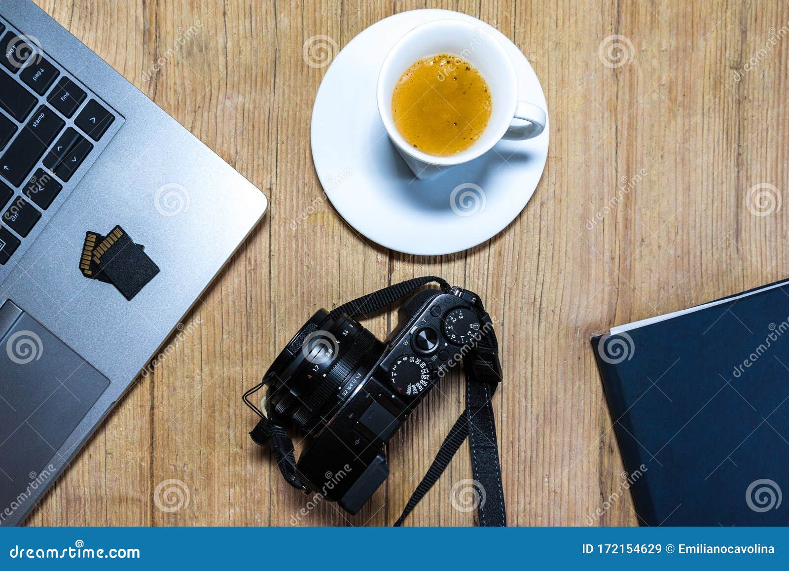 wooden desk table with camera, laptop, memory cards, espresso cup and clipboard.