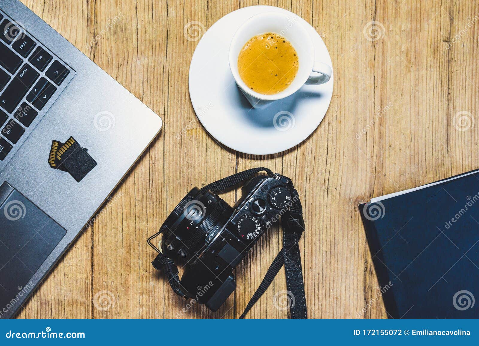 wooden desk table with camera, laptop, memory cards, espresso cup and clipboard.