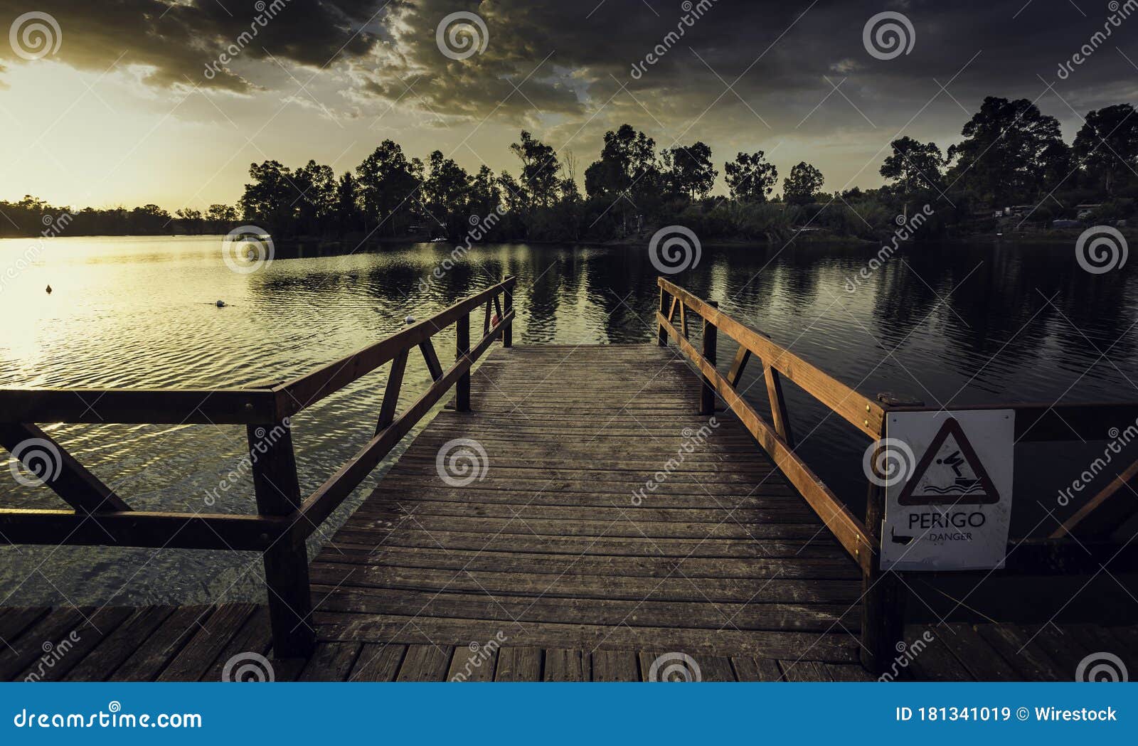 wooden dock with a [perigo - danger] sign on a river under a dark cloudy sky in the evening