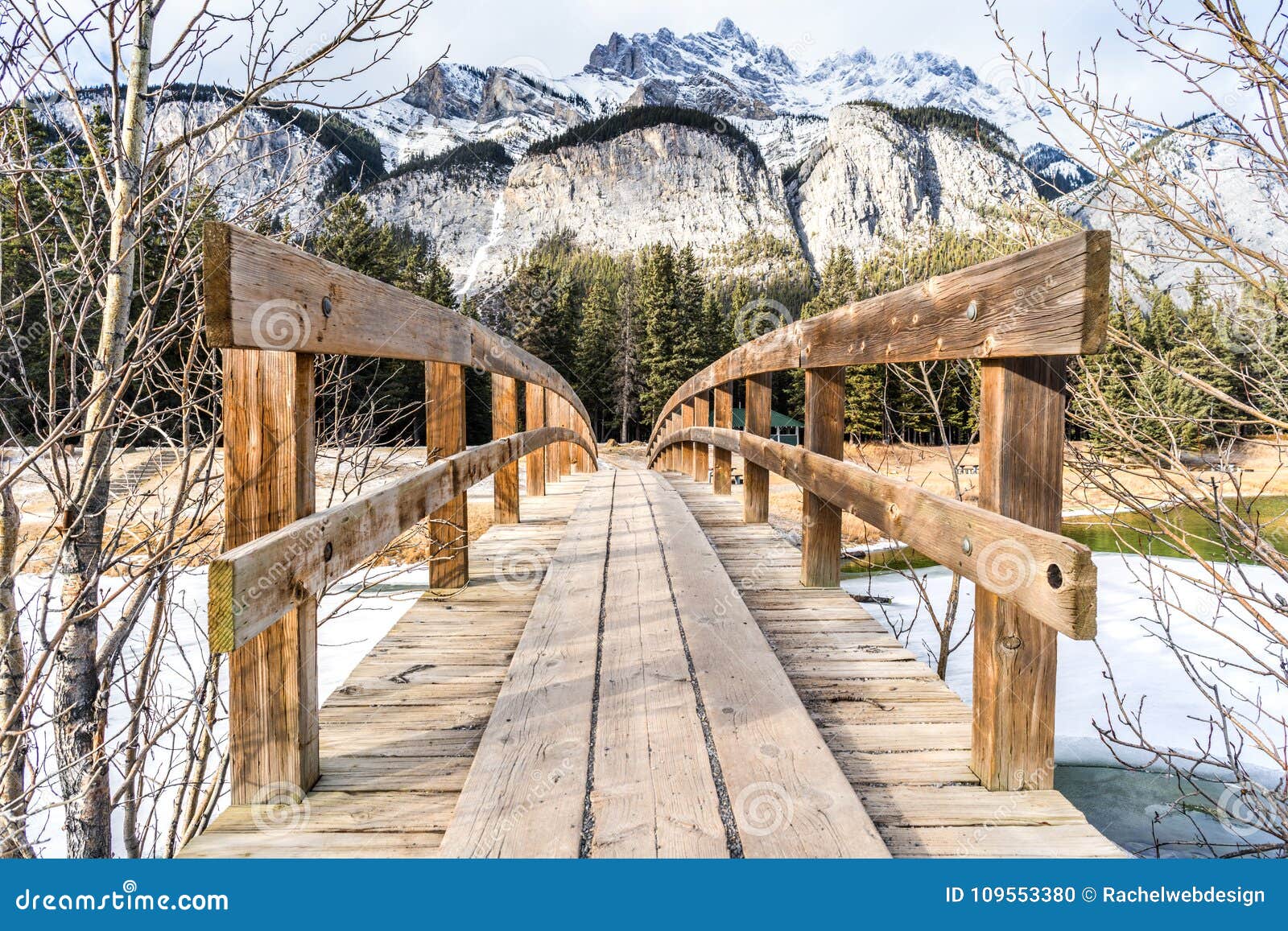 wooden foot bridge leading over glacial stream to inspiring winter mountains landscape