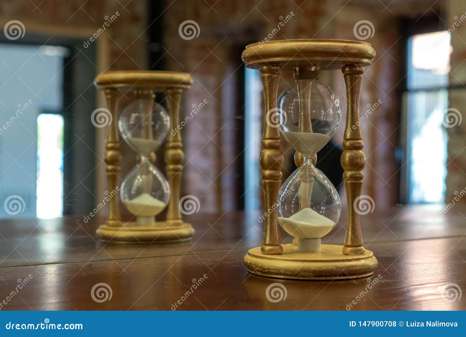 Wooden Hourglass Reflected in the Mirror. Hourglass on a Brown Table