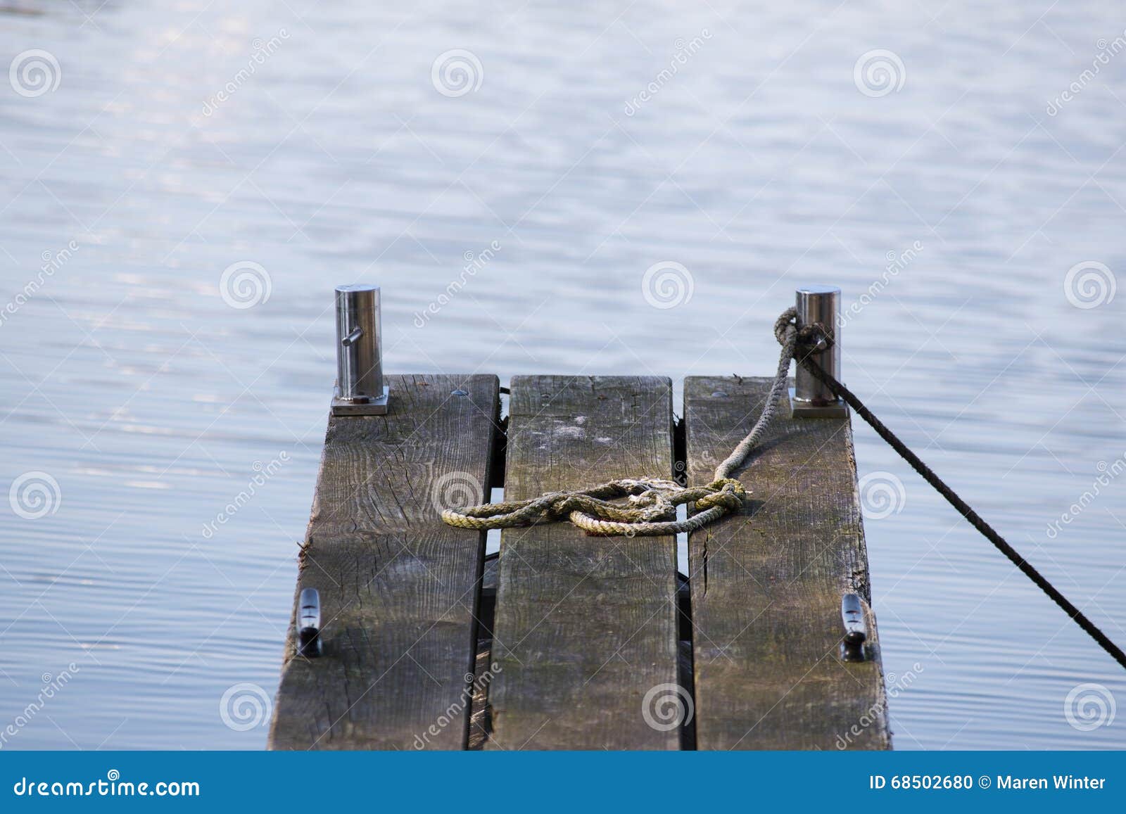 Wooden Jetty For Boats And An Old Rope In The Blue Water 