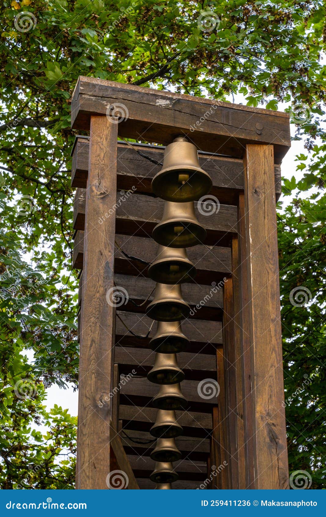 wooden rack with many brass bells and trees behind