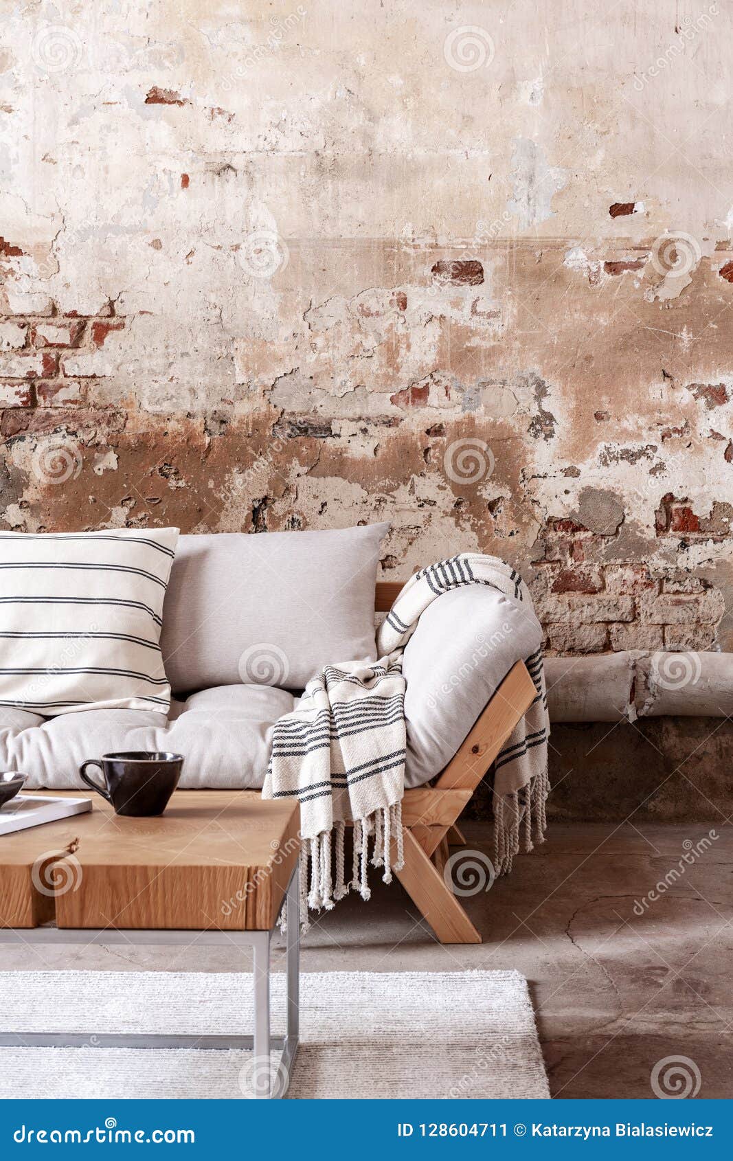 wooden table in front of grey couch with blanket in wabi sabi living room interior with red brick wall