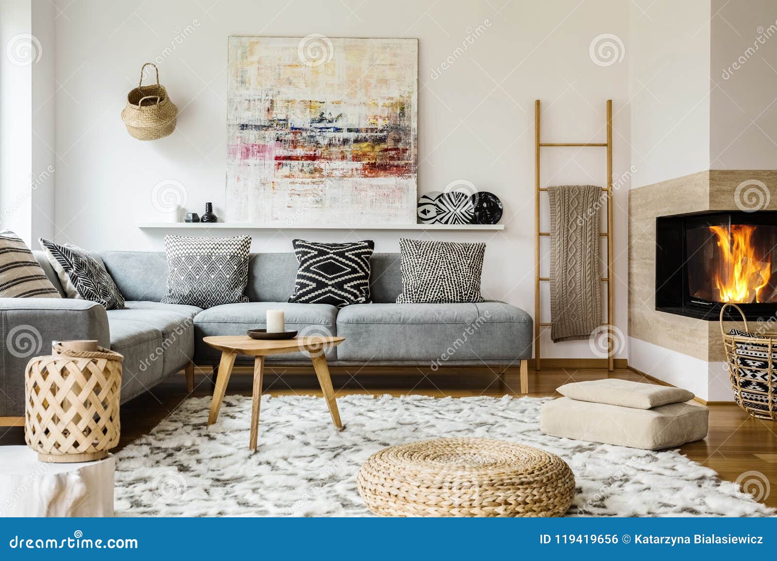 wooden table next to grey corner settee in warm living room interior with painting and fireplace. real photo