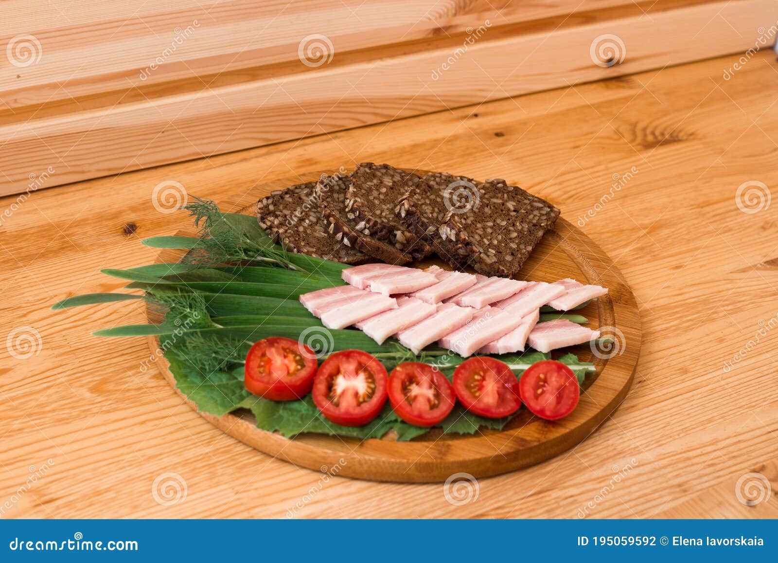 on the wooden table top is a round board with sliced black bread with seeds, smoked brisket, tomatoes and herbs