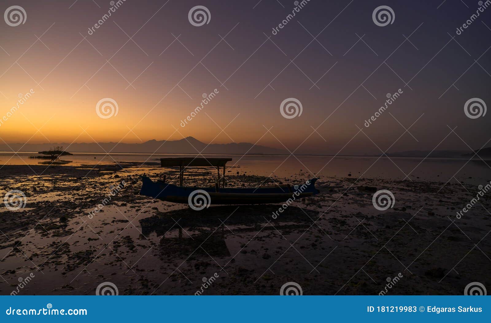 wooden traditional fishing boat stuck on low tide at the beach on vivid colorful sunset at jelenga beach, sumbawa