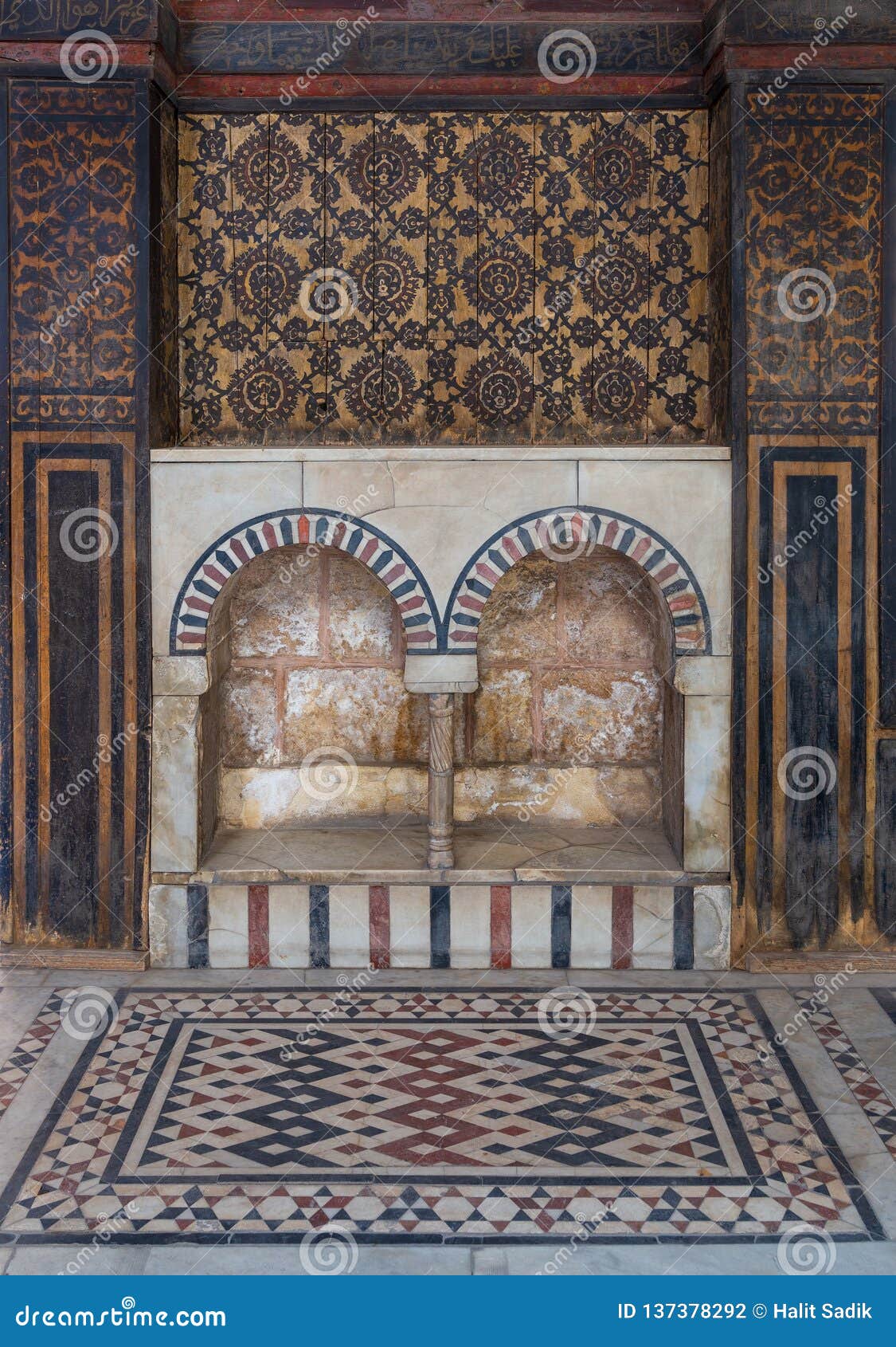 wooden wall decorated with painted floral patterns, double embedded arched niche and marble floor decorated with geometric pattern