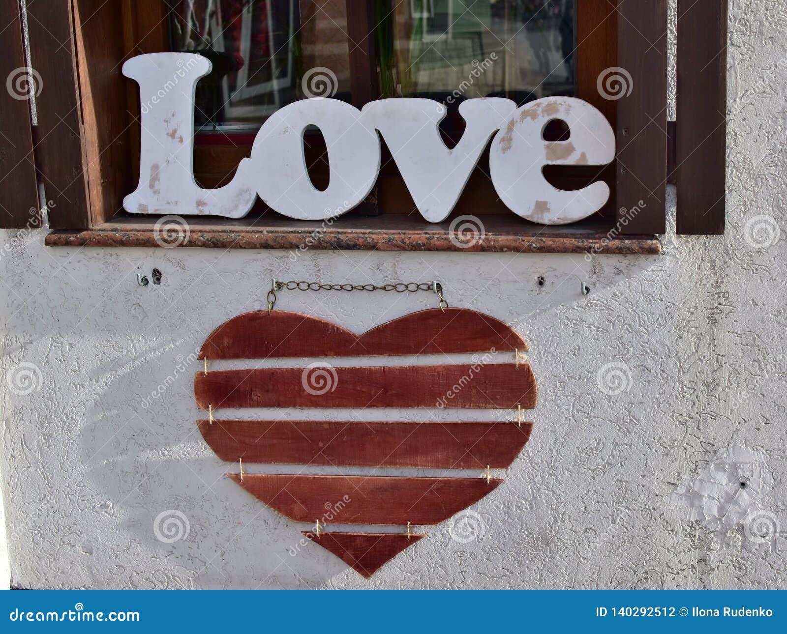 wooden word `love` standing on the windowsill and red wooden heart hanging on the wall in the city street