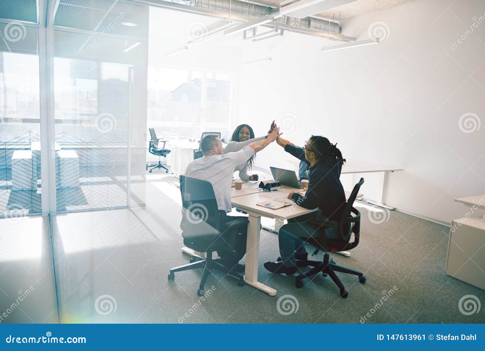 work colleagues laughing and high fiving during an office meetin