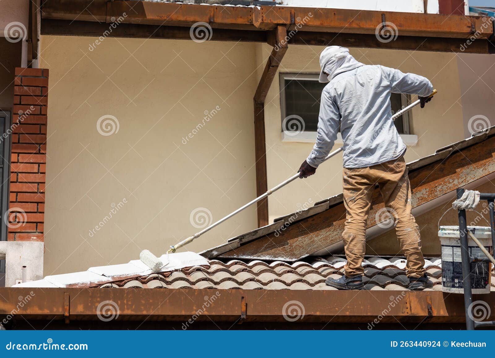 worker adding undercoat foundation paint onto rooftop with roller at residential building in renovation